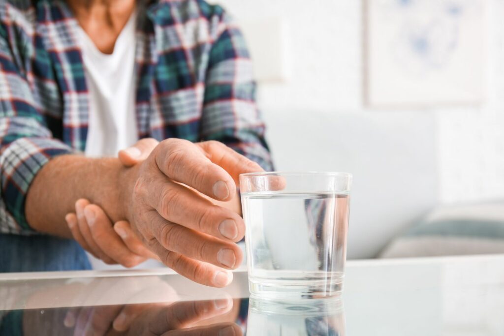 Foto de las manos de un hombre que no puede coger bien un vaso de agua por tener parkinson